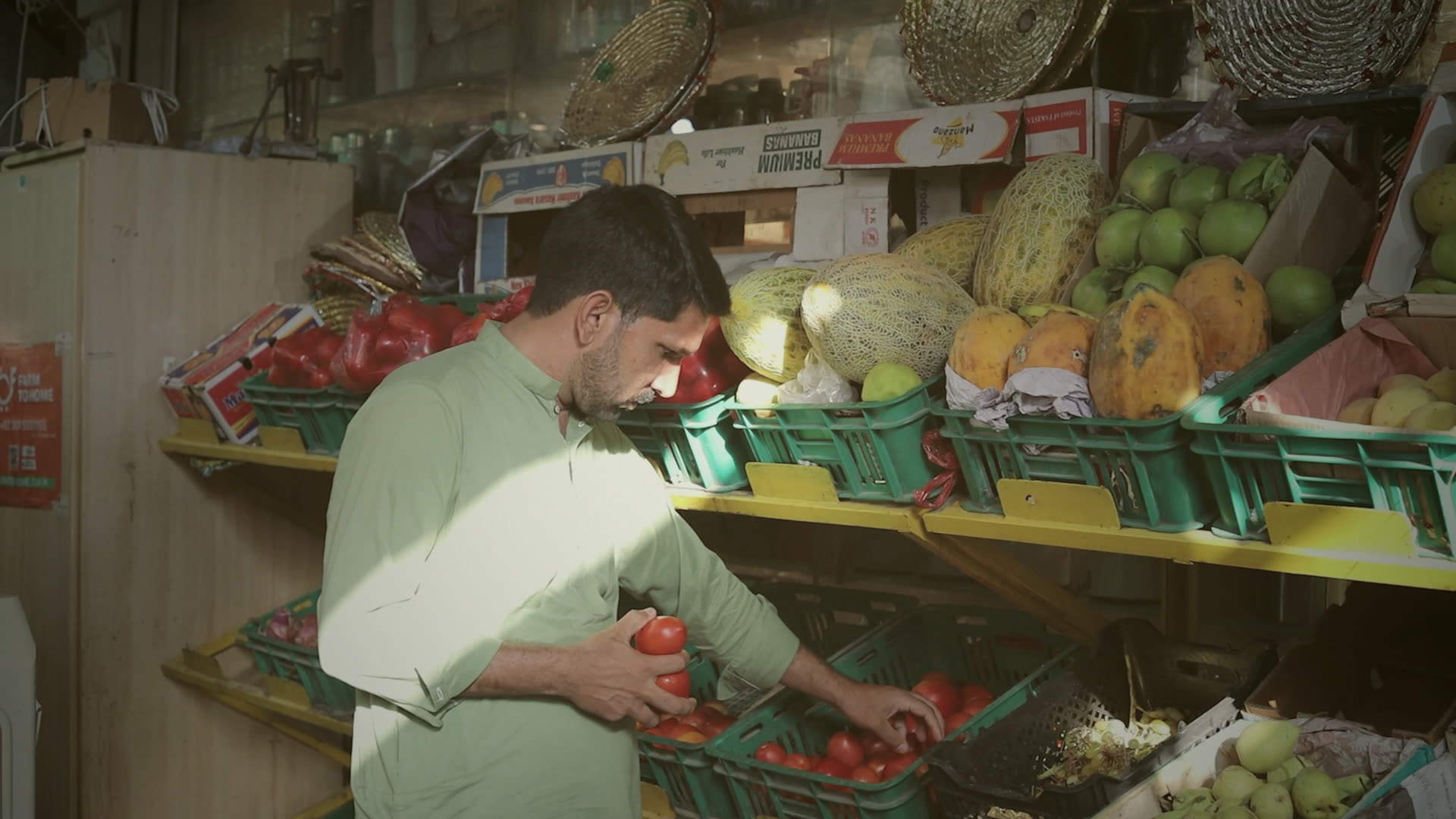 Waqas choosing vegetables from the crates at the sabzi mandi, a shaft of morning light across the stall