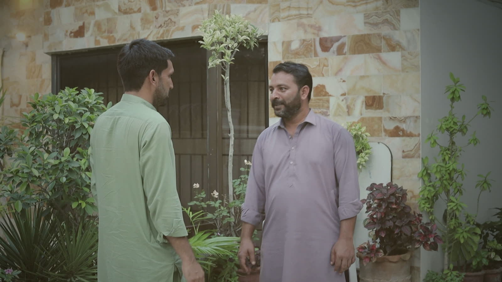 Waqas and Haider talking face to face at the stone wall of the house