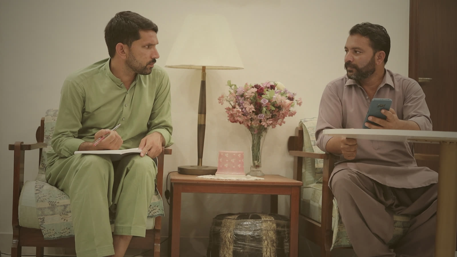 Waqas and Haider at a table indoors, a notebook open between them, planning the week
